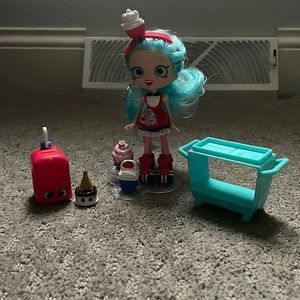 British Shopkin Doll. Comes with 3 shopkins, cart and suitcase. Great condition.